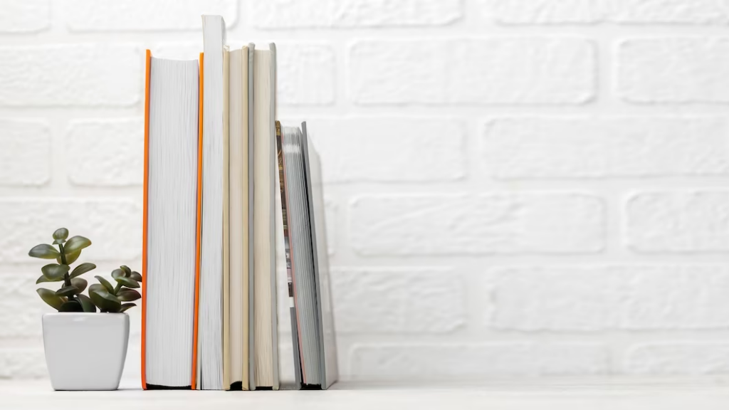 Neatly stacked books on a table with a potted plant next to them